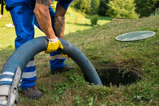 Technicien en combinaison bleue effectue vidange de fosse septique dans jardin résidentiel